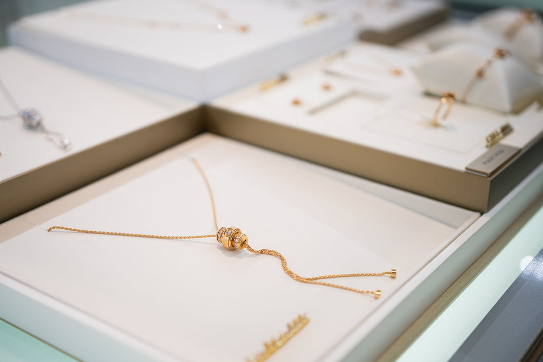 店内の什器に、金色のチェーンの先に円筒形の飾りが付いたネックレスを置いた様子。周りに他のジュエリーが並ぶ